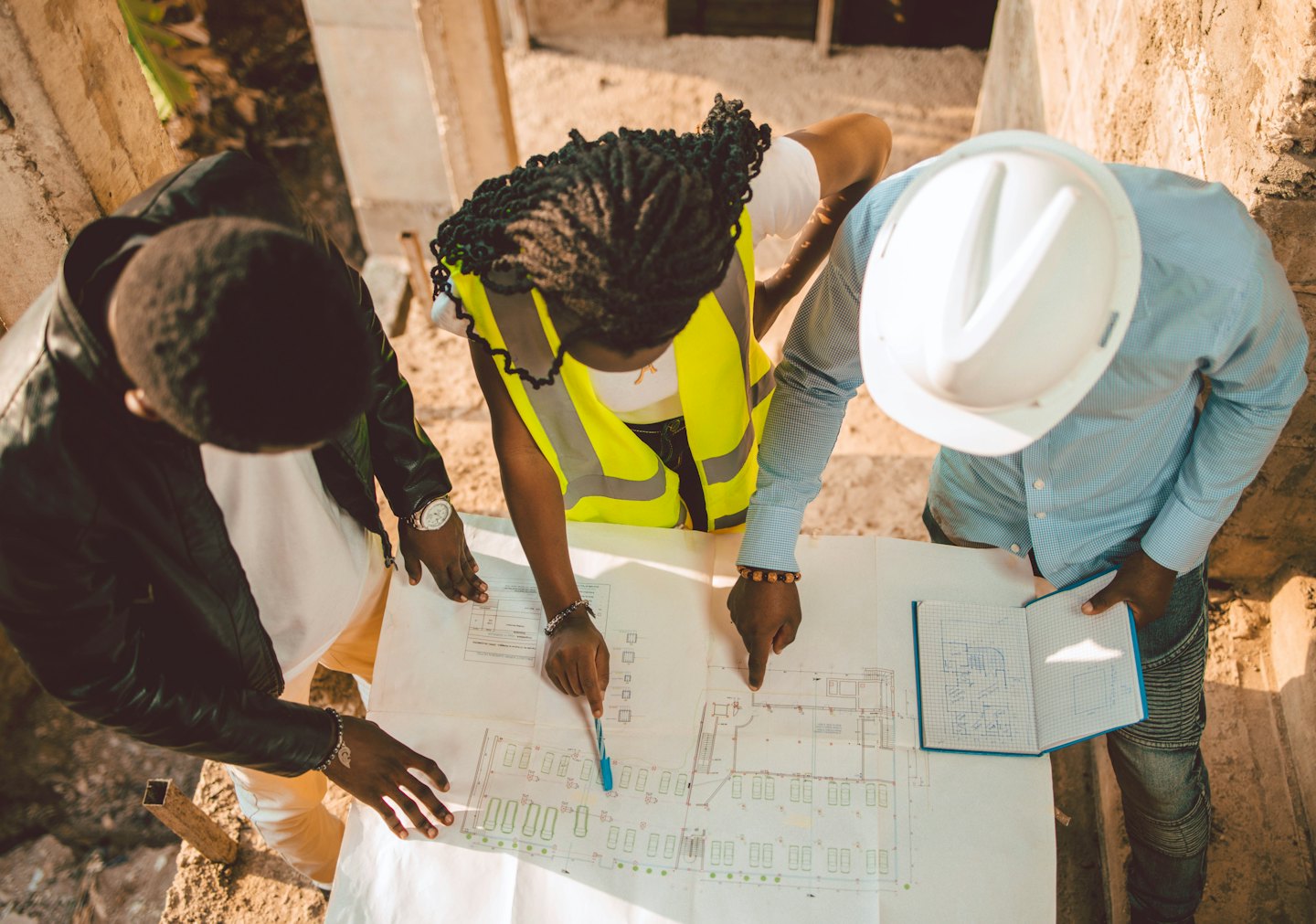 Üç inşaat profesyoneli beton bir alanda planları inceliyor.